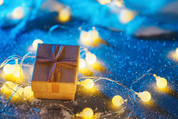 istock Christmas gift box on the table with artificial snow and glowing yellow garland 1352009511