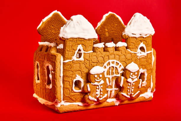 istock shortcrust pastry cookies. gingerbread house with icing decor on red background. Concept of winter traditional dessert - side view 1352010195