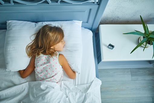 Little girl sleeping on a big and cozy bed white linen in the afternoon at home, family lifestyle, comfortable pillow, bed, healthy sleep of children, melatonin, cyrcadian rhythms concept