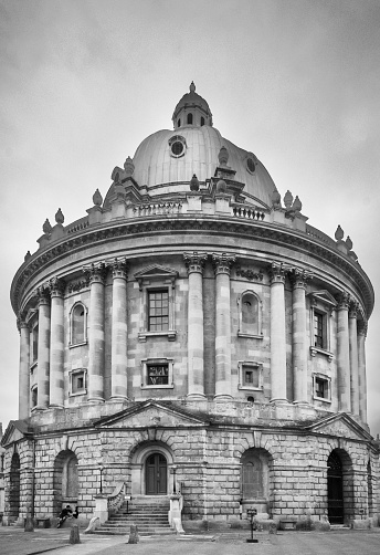 The famous Radcliffe Camera building in Oxford, Oxfordshire, England, UK, with tourists in the foreground and an overcast sky.