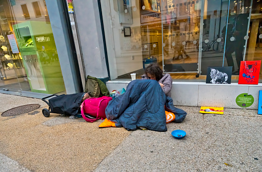 A homeless person on the streets of Oxford. She is a young woman in a sleeping bag as her makeshift home outside a clothes shop on Broad Street half asleep with a begging bowl.