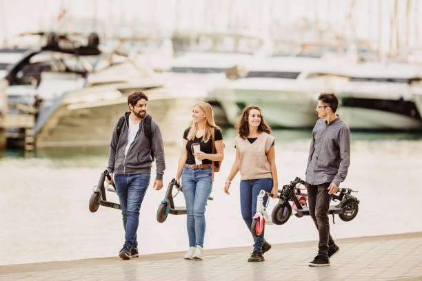 istock Four young smiling people walking with their folded motorised scooter in the harbor 1352016873