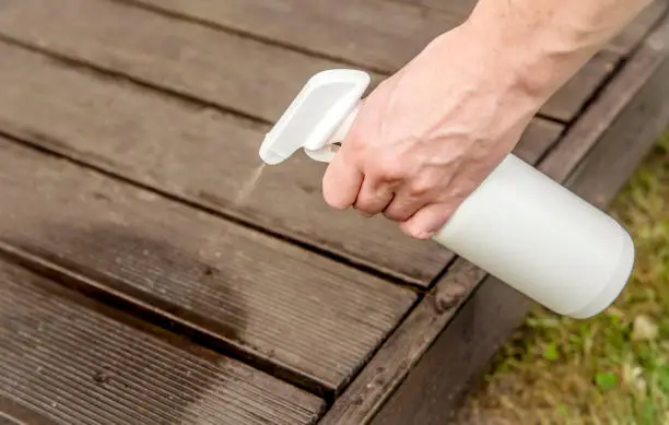Photo of Homemade ant repellent spray mixture in bottle. Person hand spraying insect repellent on home terrace wood boards.