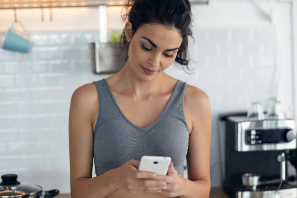 istock Sporty young sporty woman using mobile phone while taking a break standing in the kitchen at home. 1352018194
