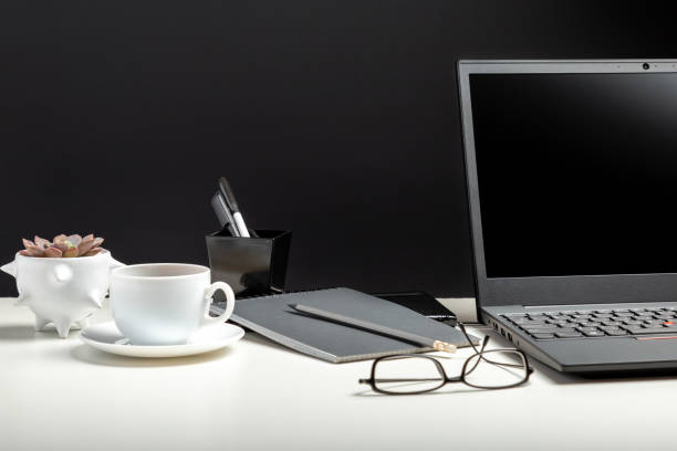 istock White table with laptop, coffee glasses for remote work or study. Black laptop with blank display layout template on black background. Office pc desk workspace in Home Office interior with copy space 1352019909