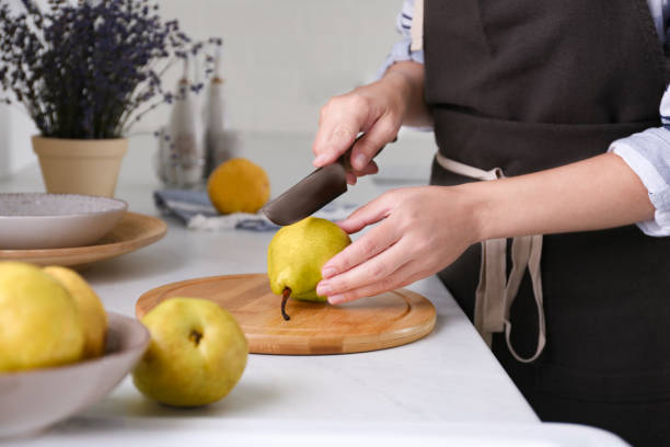 Woman cutting fresh ripe pear at table in kitchen, closeup