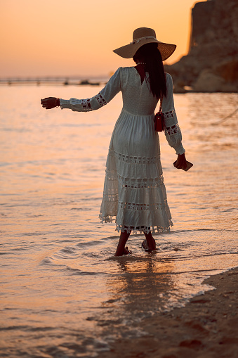 Beautiful african woman in sun hat walks on beach at sunset. High quality photo