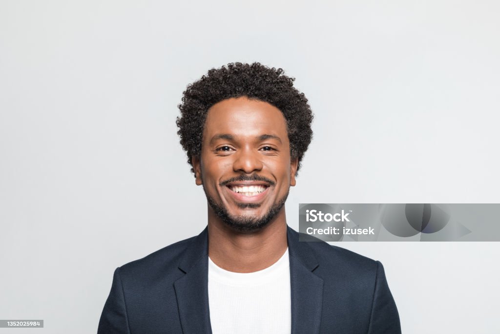 Headshot of cheerful young businessman Portrait of mid adult man wearing suit and white t-shirt, smiling at camera. Studio shot of male entrepreneur against grey background. Men Stock Photo