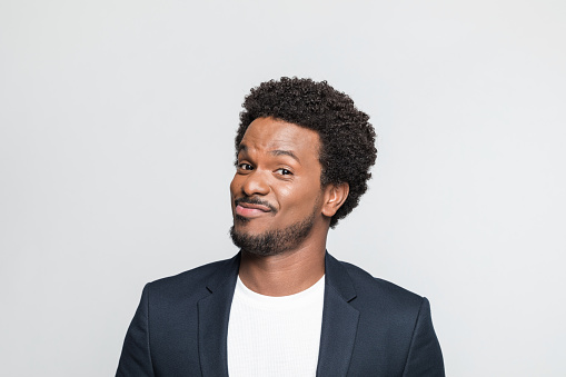 Portrait of mid adult man wearing suit and white t-shirt, smiling at camera. Studio shot of male entrepreneur against grey background.