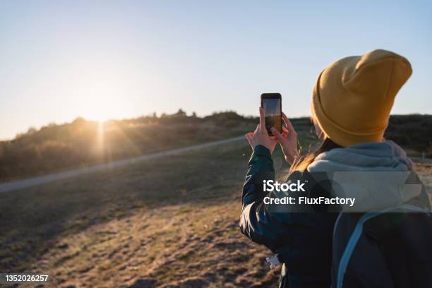 While Looking At The Majestic View Serene Woman A Hiker Taking A Photo Of Susnet Above Nature With Mobile Phone Stock Photo - Download Image Now