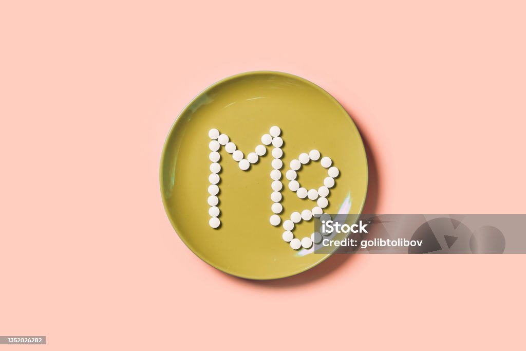 MG text. Symbol of magnesium on plate Pills with mineral Mg or magnesium on yellow plate. Mg inscription made of medical pills Magnesium Stock Photo