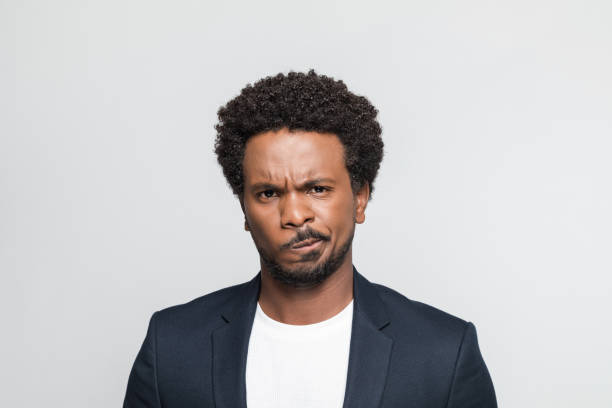 Headshot of displeased young businessman Portrait of mid adult man wearing suit and white t-shirt, staring at camera. Studio shot of male entrepreneur against grey background. frowning stock pictures, royalty-free photos & images