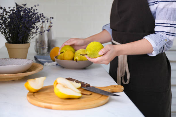 Woman holding fresh ripe pear in kitchen, closeup