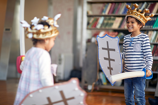 A little brother and sister dressed like knights are ready for swords fight game while playing in a cheerful atmosphere at home. Family, home, playtime