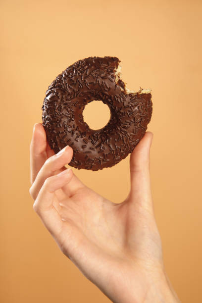 istock hand holding bitten chocolate donut isolated on brown background 1352034313