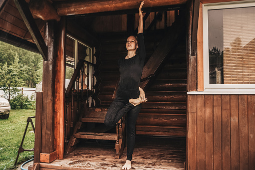 Young woman doing yoga in veranda of a wooden house.