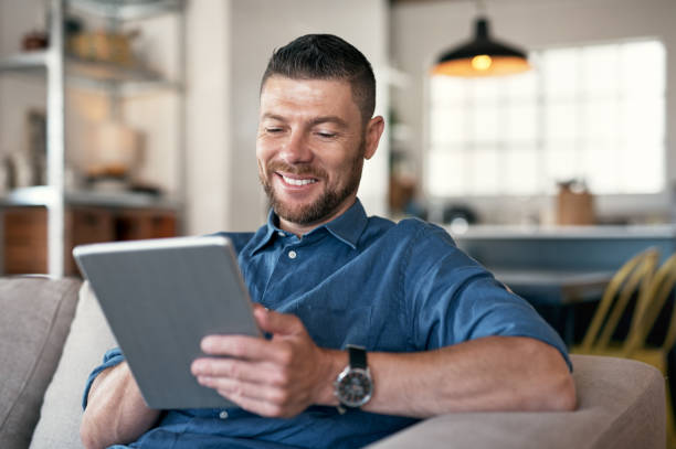 istock Shot of a handsome man relaxing on his sofa using a digital tablet 1352037813