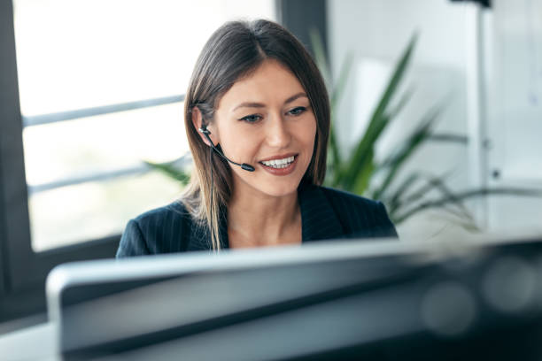 istock Attractive business woman making video call with computer while talking with earphone sitting in modern startup office. 1352045038