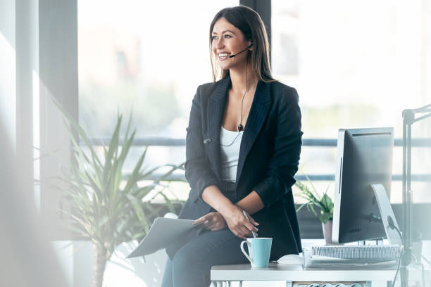 istock Elegant business woman talking with earphone while checking some documents in modern startup office. 1352046342