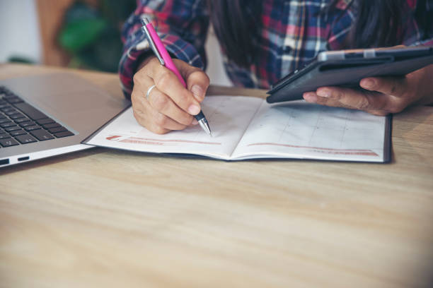 istock Planner or organizer writing daily appointment On Calendar book and using tablet. Hand of Asian woman plan timetable meeting agenda and note schedule business on the diary. Planner concept. 1352047519