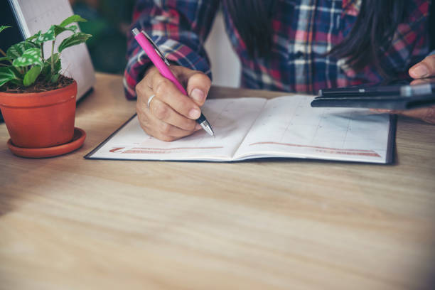 planificador u organizador escribiendo citas diarias en el libro de calendario y usando tableta. mano de la mujer asiática planificar el horario de la agenda de reuniones y anotar el horario de negocios en el diario. concepto de planificador. - working at home calendar laptop women fotografías e imágenes de stock