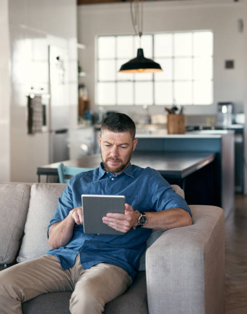 istock Shot of a handsome man relaxing on his sofa using a digital tablet 1352049025