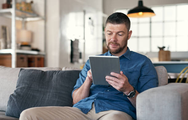 istock Shot of a handsome man relaxing on his sofa using a digital tablet 1352049042