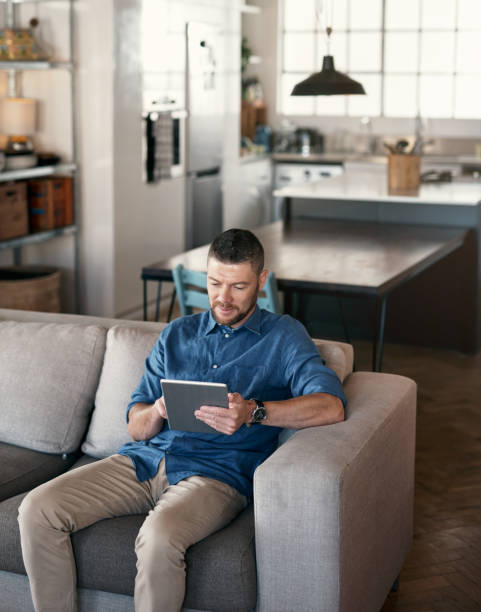 istock Shot of a handsome man relaxing on his sofa using a digital tablet 1352049048
