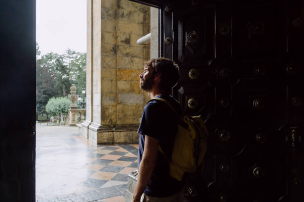 istock Panoramic view of young man with backpack sightseeing in a religious basilica in Spain. 1352049315