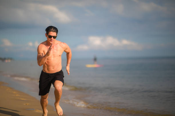 giovane che corre sulla spiaggia - men beach running shirtless foto e immagini stock