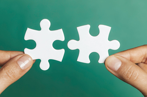 Two hands are holding puzzle pieces in front of green background.