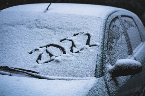 Snow on the car where the numbers are written 2022. Travelling by car.