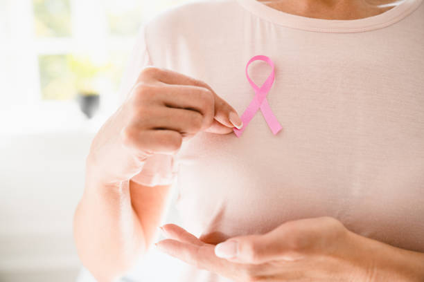 femme caucasienne en t-shirt rose faisant de la palpation avec un ruban rose sur sa poitrine pour soutenir la journée mondiale du cancer du sein. lutte contre les tumeurs, récupération de l’oncologie - breast cancer breast cancer awareness ribbon social awareness symbol human hand photos et images de collection