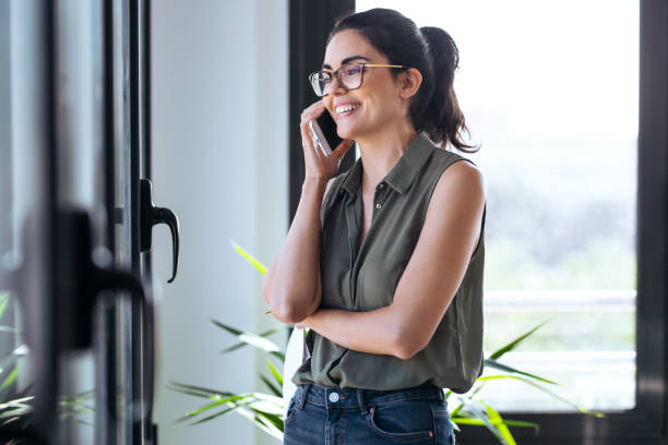 istock Beautiful woman using her mobile phone while standing next to the window at the office. 1352063450