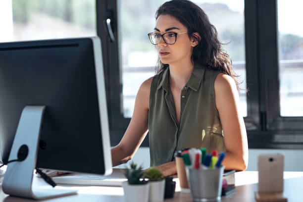 joven empresaria concentrada que trabaja con computadora en la oficina. - usando el ordenador fotografías e imágenes de stock