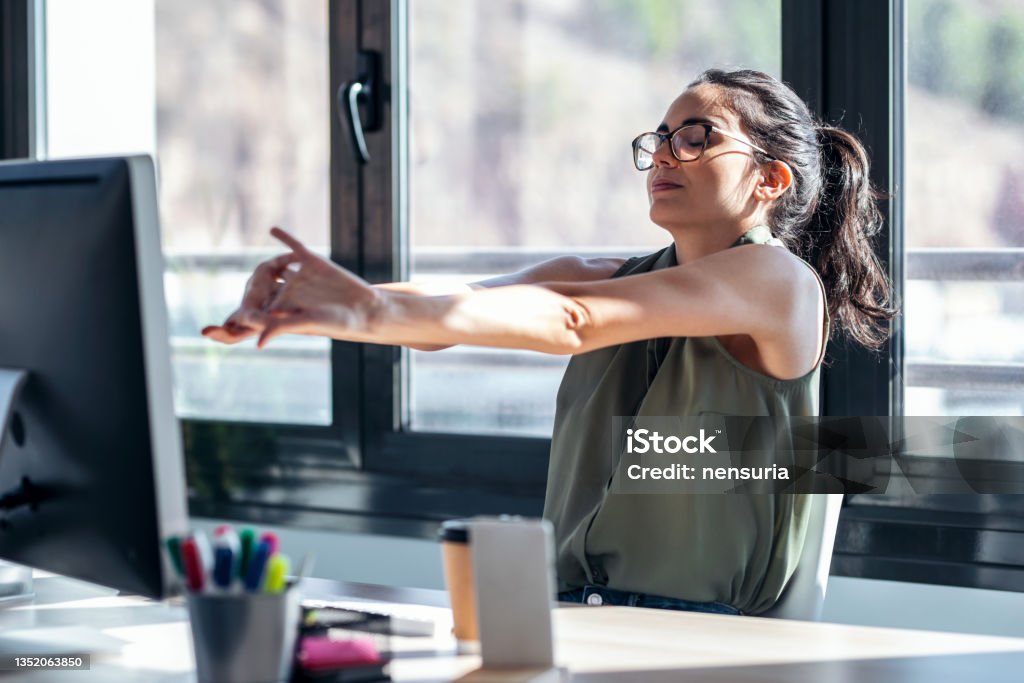 Tired businesswoman stretching body for relaxing while working with computer in the office. Shot of tired businesswoman stretching body for relaxing while working with computer in the office. Stretching Stock Photo