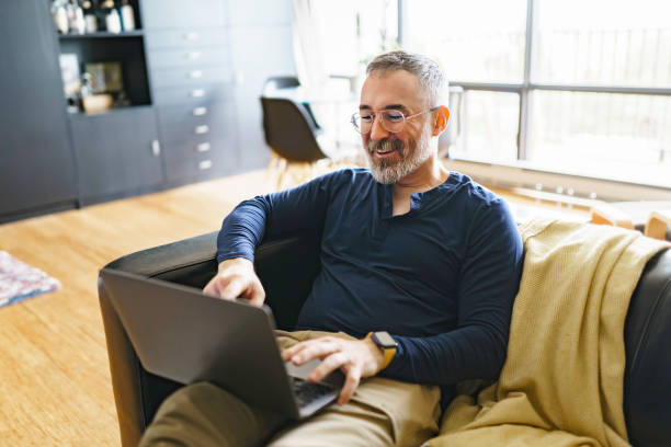retrato de hombre guapo con computadora portátil en el sofá - gente tranquila fotografías e imágenes de stock