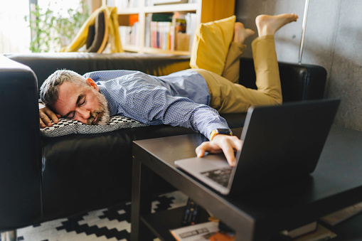 Hombre maduro sintiendo estrés y cansado de la computadora se a tuyó en el sofá con una computadora portátil al frente photo