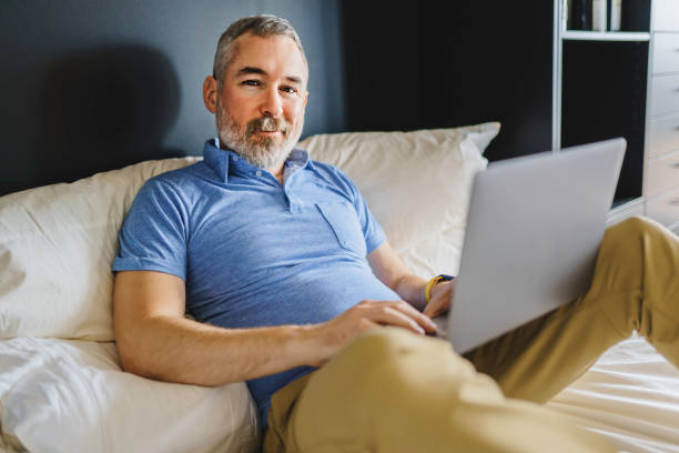 istock nice mature man at hotel with grey beard relaxing on bed with laptop 1352064316