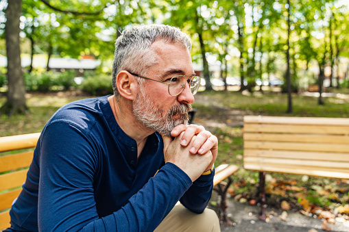 A Portrait of a mature man sitting on a bench in an urban park