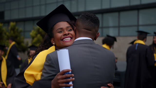 Happy African American graduate student hugging her father on graduation day while holding her diploma