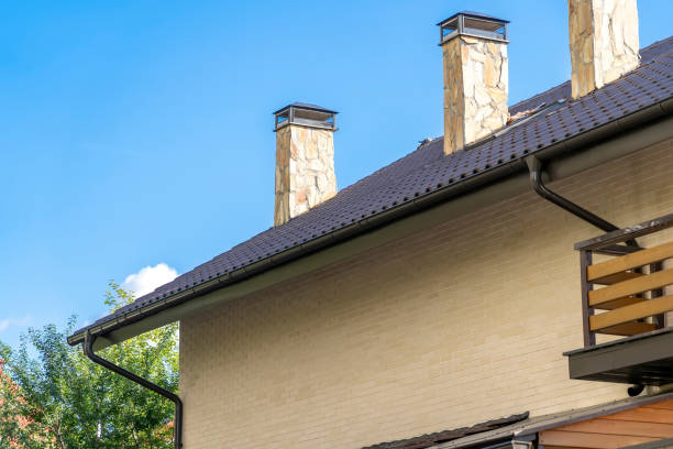 Brick house with drainage system on metal roof. Сhimney pipes is finished externally with natural stone. Roof gutter pipeline system. House rain gutter with holders and downspout pipe against blue sky. casa de ladrillo con sistema de drenaje en techo metálico. las tuberías de Сhimney están terminadas externamente con piedra natural. sistema de tuberías de canaletas de techo. canaleta de lluvia de la casa con soportes y tubo de bajantes contra el cie