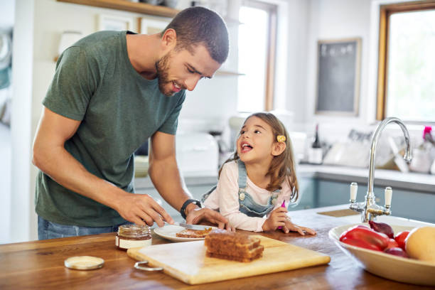 Man standing with daughter while making sandwich Girl talking to father making sandwich. Mid adult man is standing with daughter while preparing breakfast. They are in kitchen at home. peanut butter and jelly sandwich stock pictures, royalty-free photos & images