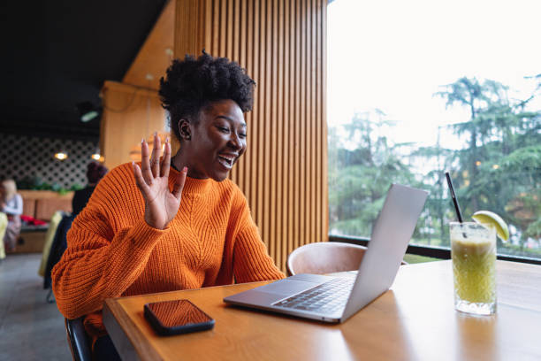 Modern female freelancer of Black ethnicity wave back during a business video call on laptop stock photo