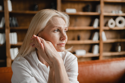 Stressed sad tired exhausted caucasian middle-aged mature businesswoman freelancer relaxing on the couch sofa, thinking about family marriage work problems at work office