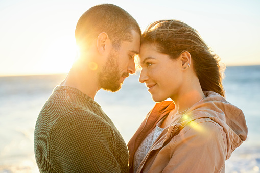 Romantic couple standing face to face by sea. Male and female are spending leisure time together. They are at beach.