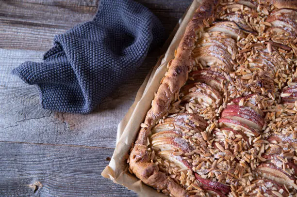 Homemade fresh baked sheet cake with yeast dough. Topped with sliced apples and almonds and served on a baking sheet from above. Isolated view with copy space
