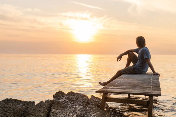 istock Young man relaxing on pier at sunset 1352070956
