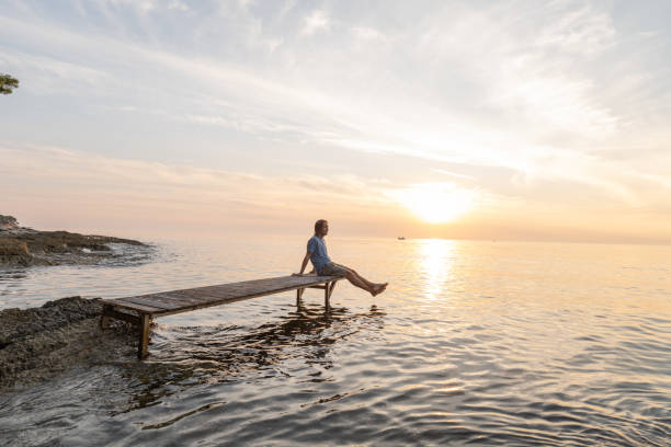 istock Young man relaxing on pier at sunset 1352071252