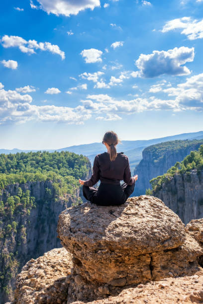 Unrecognizable woman meditating on edge of cliff